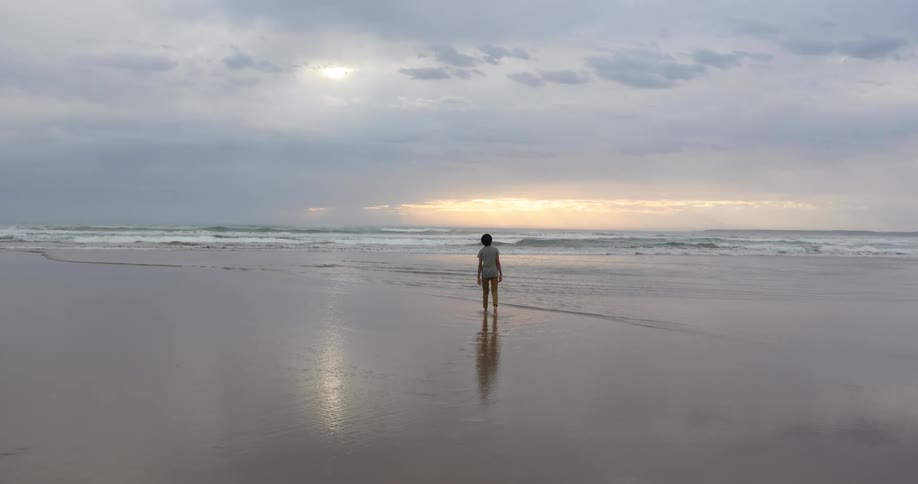 A person walking over the wet sand on a beach next to the ocean at sunset