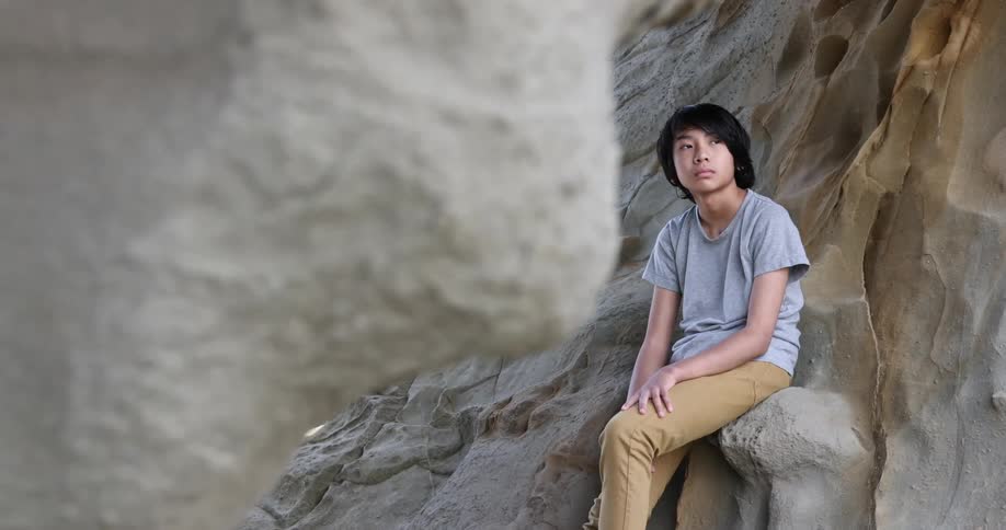 A boy sits leaning against a rock canyon wall