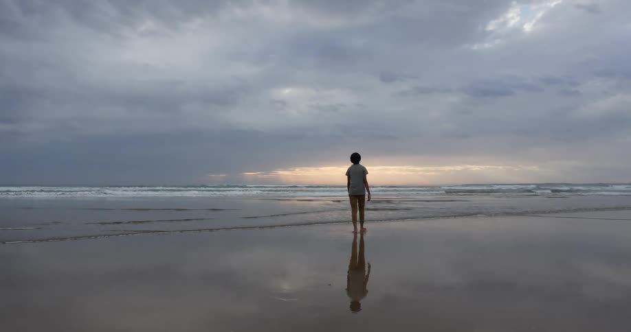 A person is walking on the beach on a cloudy day