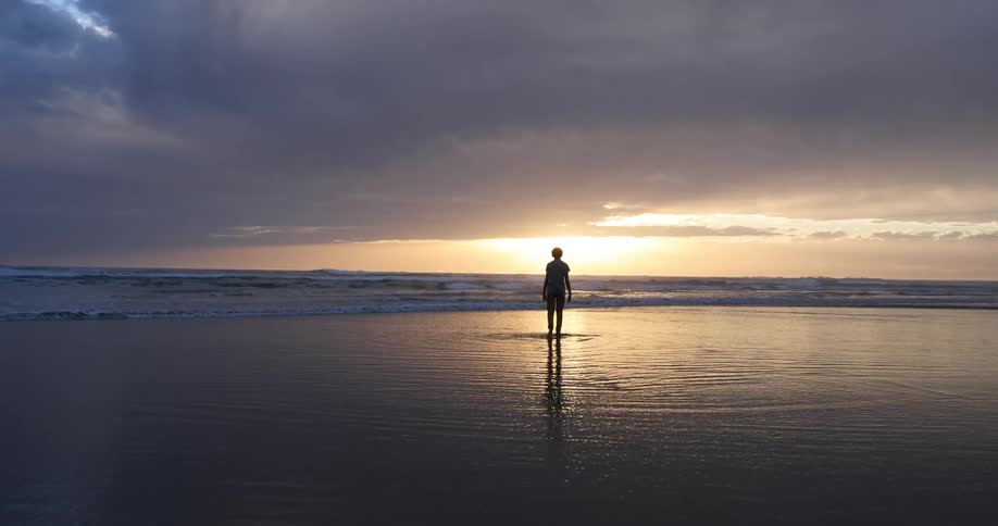 The silhouette of a person wading towards the waves at sunset