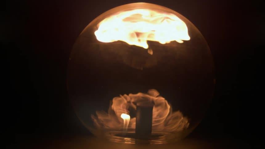 Flames shoot out of a tube and are contained in a clear globe in the darkness
