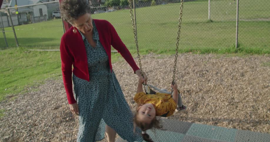 An elderly grandma pushing her granddaughter on an outdoor swing in summer