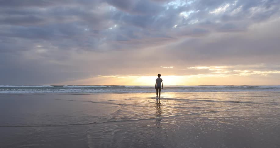 A person on the shore walks out in to the water as the sun sets