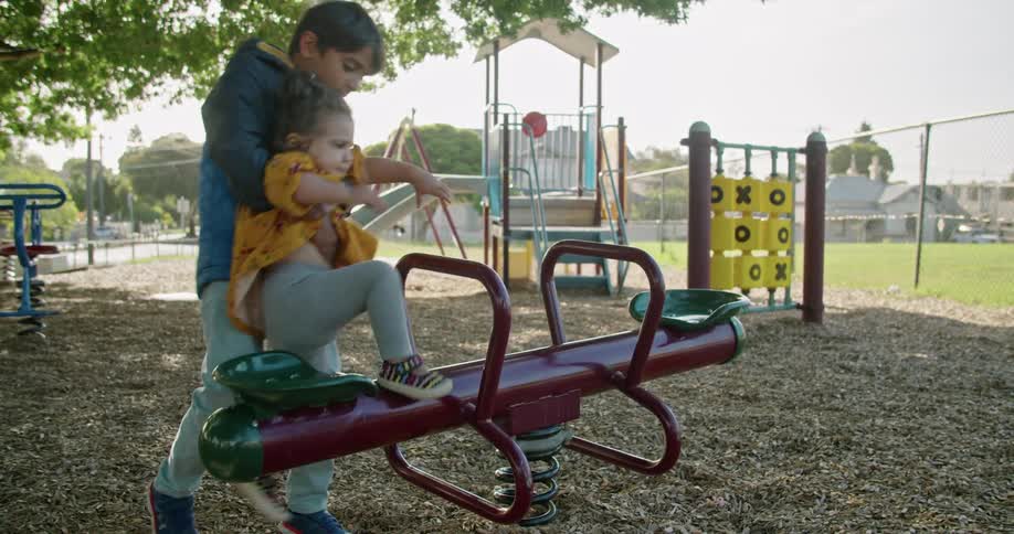 Brother helps little sister to sit on the seesaw in the playground