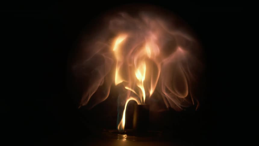 Fire explodes from a candle and the flames are contained inside a clear globe in the darkness