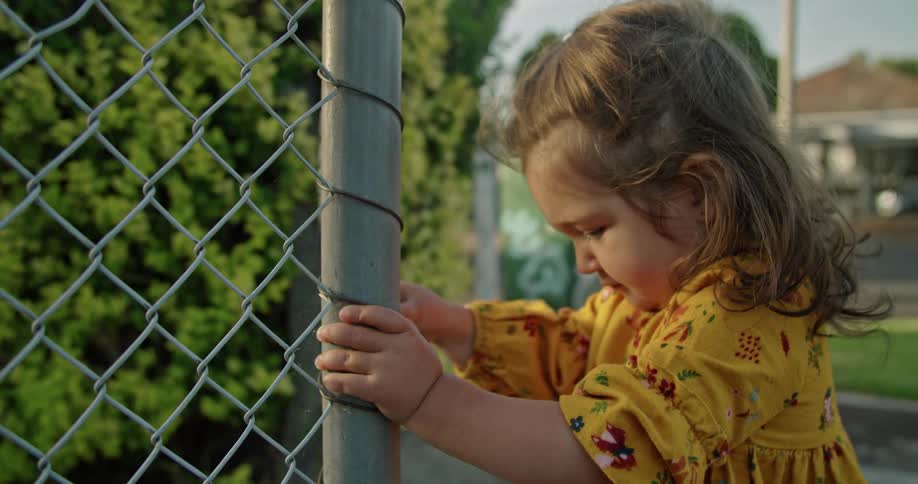 A toddler girl pulling on a chain link fence outside