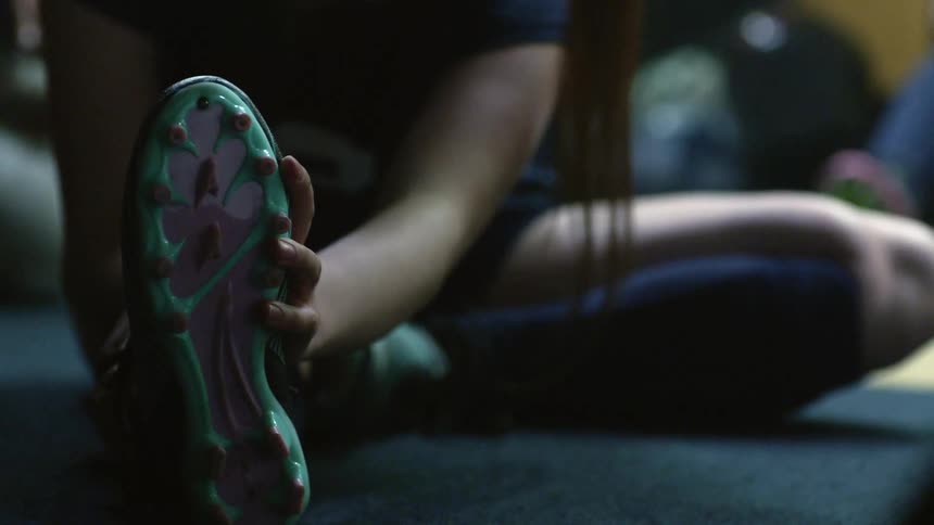 Young woman wearing a sports uniform stretching on the floor of a locker room