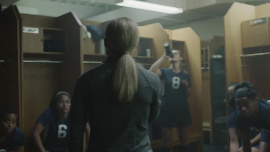 A woman coach in the locker room talking to girls in a sports team wearing uniforms