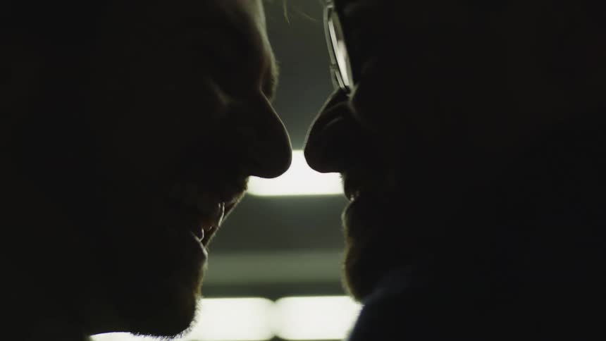 Two men smile and kiss outside at night