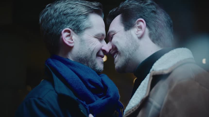 Two men smiling while kissing in the dark