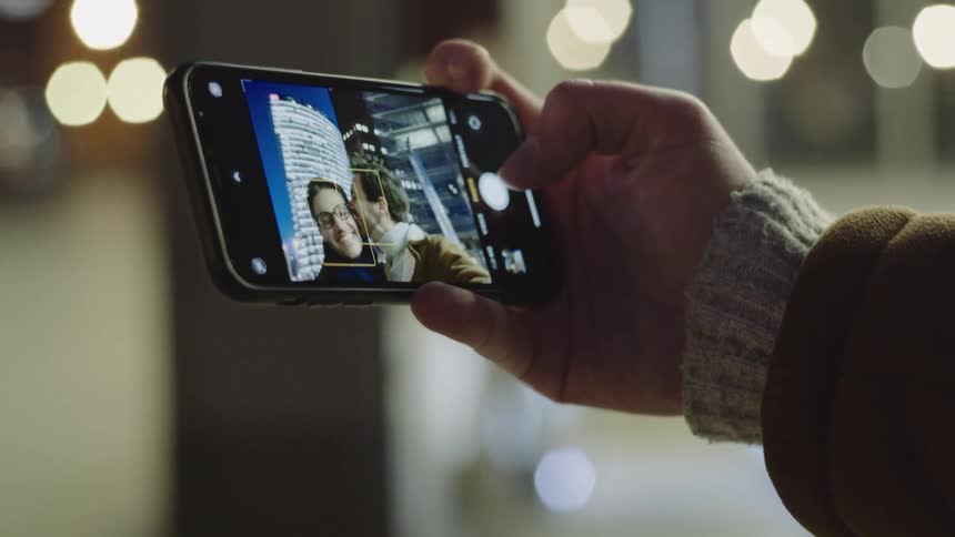Male couple smiling and kissing while taking a selfie in the city at night