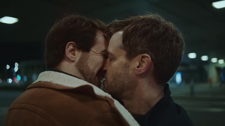 Two men kiss and hug at night
