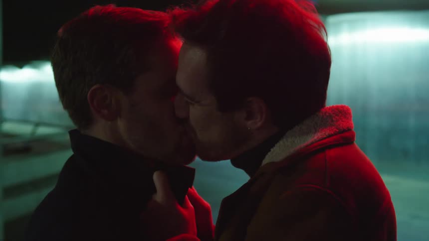 Two men are kissing and standing outdoors at night