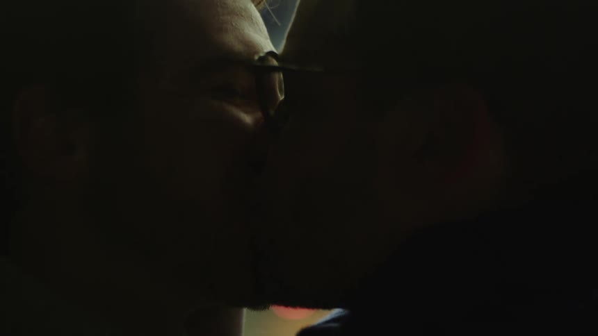 Two men smile and kiss with city and traffic lights behind them