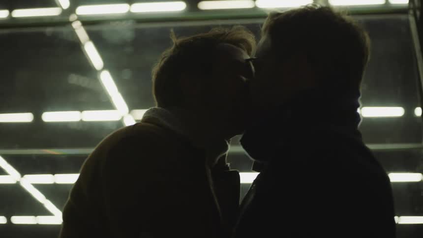 Two men kiss outside on a windy day