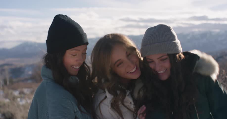 Three women stop to take selfies on a smartphone while on a hike near a mountain range