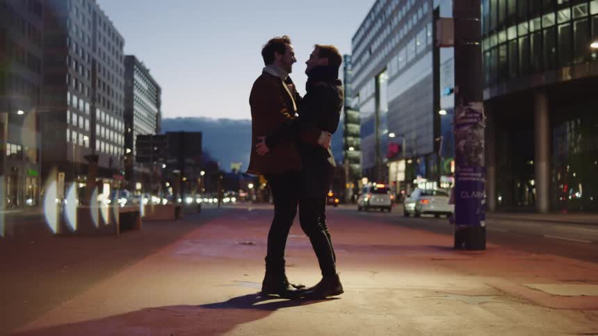 Two males standing near traffic hugging and kissing