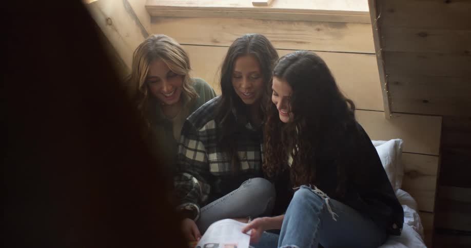 Three women in a room sitting and looking at a magazine with a wall in the background