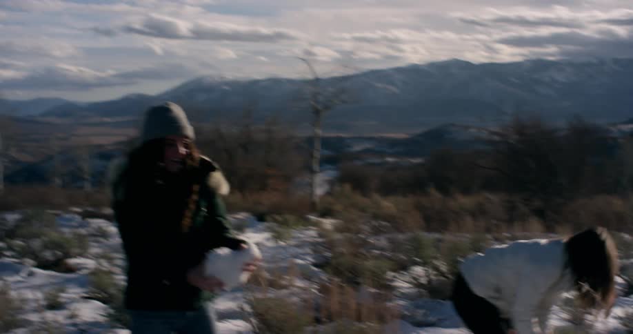 Three women with hats and coats throwing snowballs at each other with the sky and clouds in the background