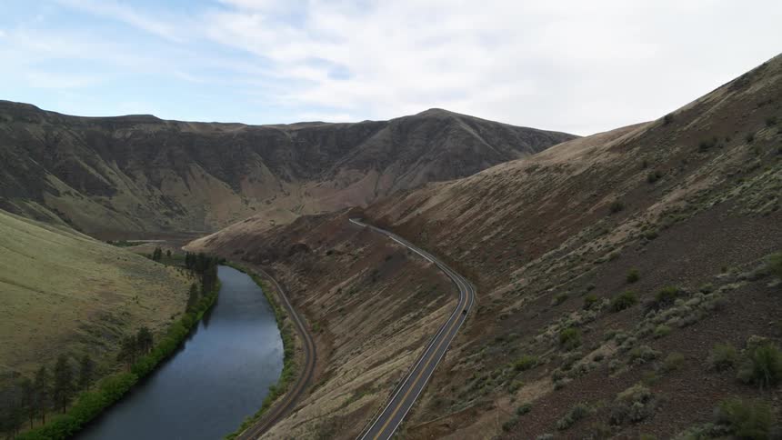 Wide view of a vehicle driving down the road in a rural river canyon