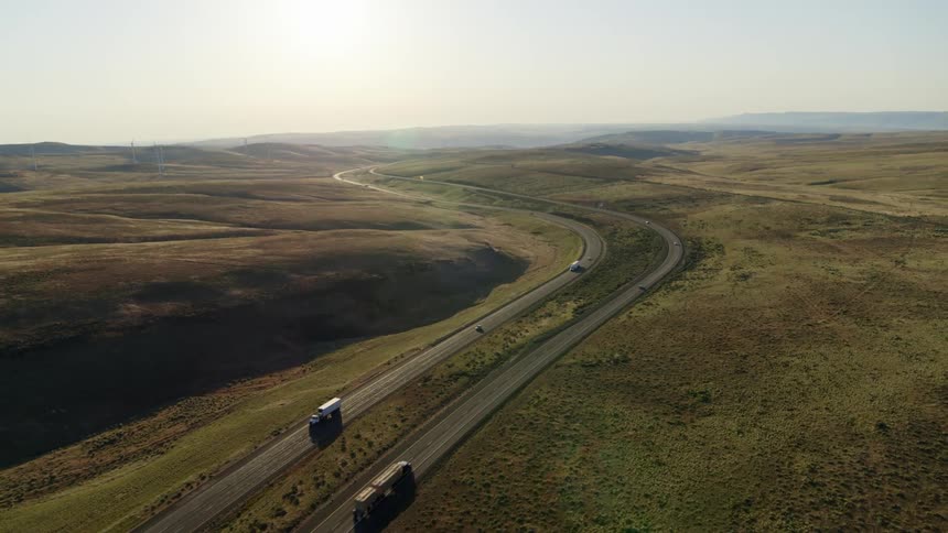 Cars and trucks drive along a winding stretch of interstate highway through open grassland
