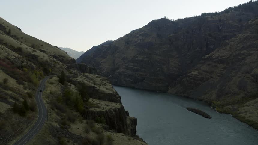 A car travels on a treacherous canyon road with steep drop offs down to a river below