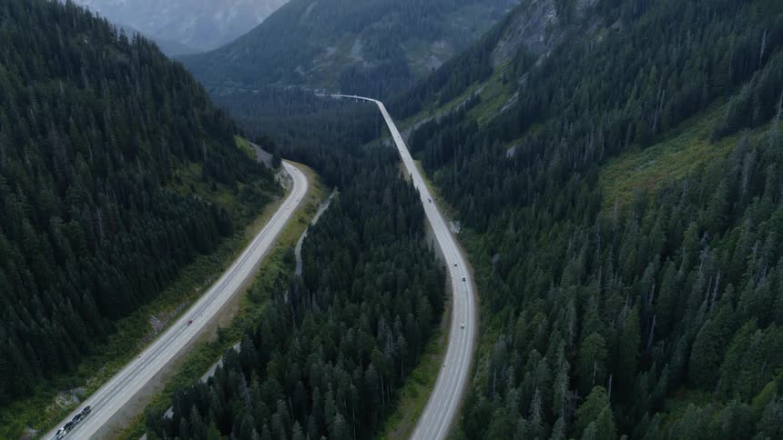 An interstate highway winds through a mountain pass surrounded by various peaks and evergreen forest