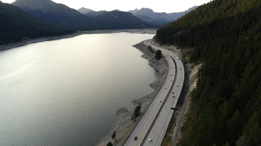 Cars and trucks travel along a highway next to a beautiful mountain lake