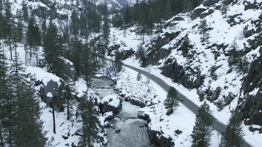 A car drives down a beautiful mountain road near an icy river