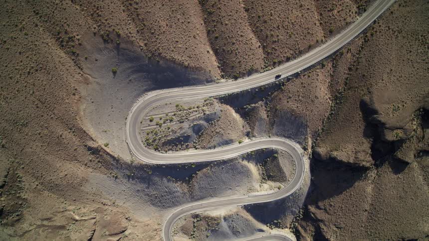 A car drives along a winding road with sharp serpentine curves on a scuplted mountainside