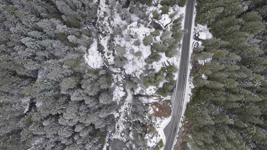 Cars driving down a narrow mountain highway near an icy river gorge and frost covered forest