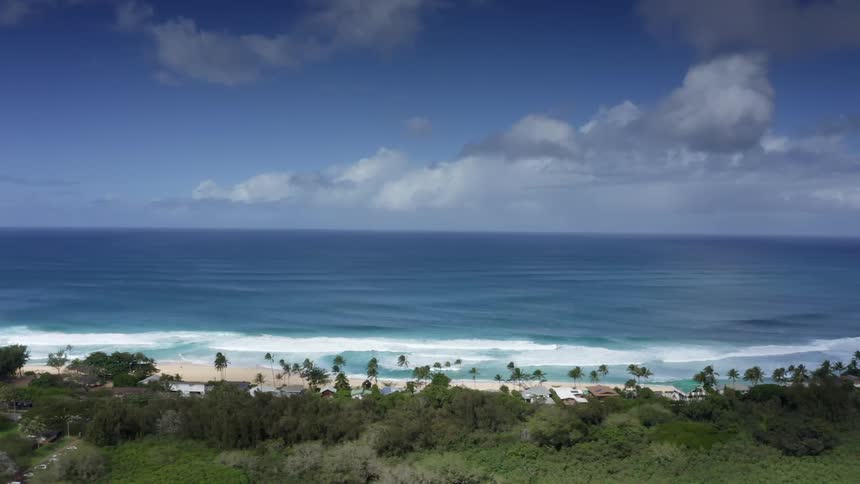 Waves roll across beach with trees and houses along the coastline
