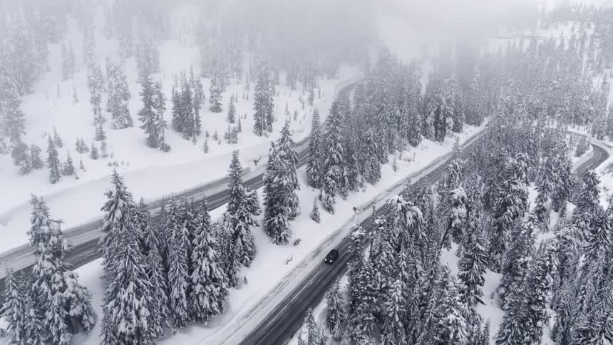 A car travels on a winding mountain road through a misty snow covered forest