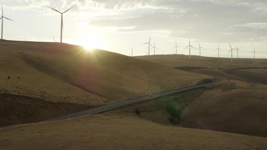 A car travels on a rural highway past wind turbines