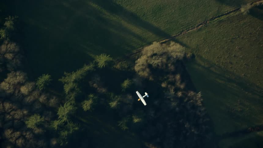 A single engine Cessna Airplane flies low underneath the camera and out of frame in this high altitude aerial