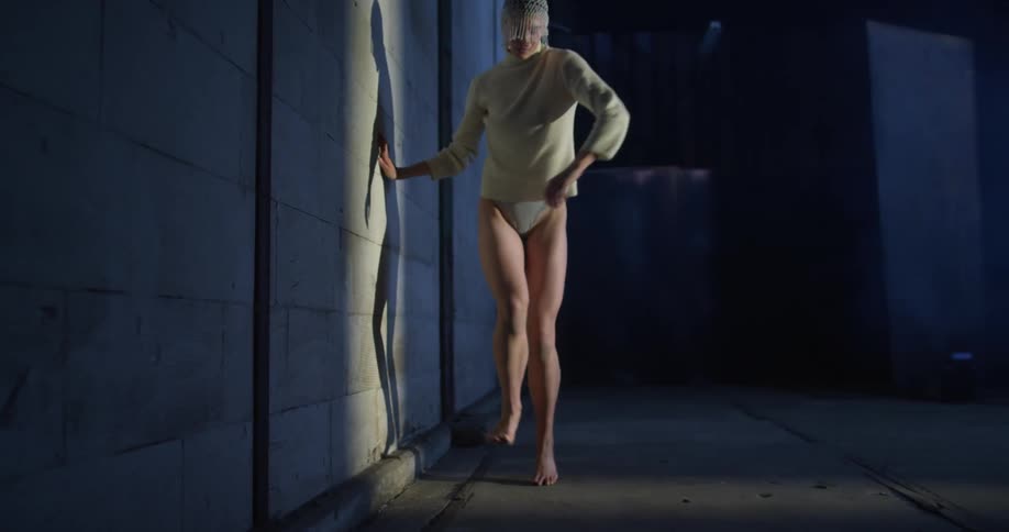 Woman performing modern dance projecting a shadow in the wall of a dimly lit abandoned warehouse