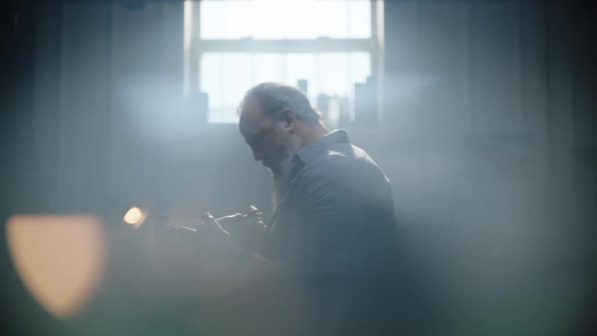 A man in a room looking at a tool with a wall and a window in the background