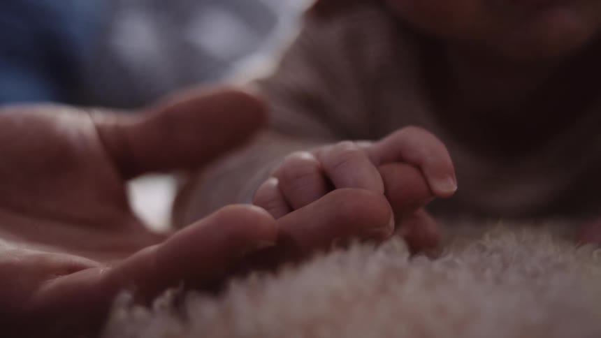 Man holds babys hand lying on the carpet