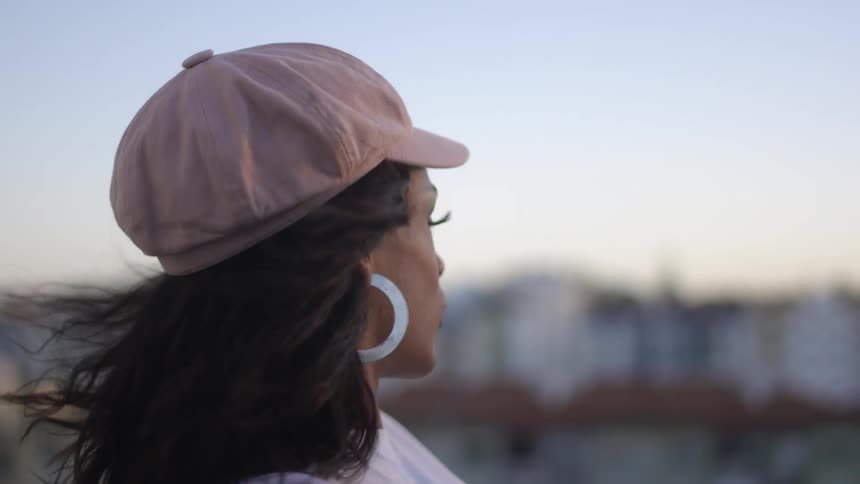A woman standing in profile turns her head as she poses while the wind blows her hair
