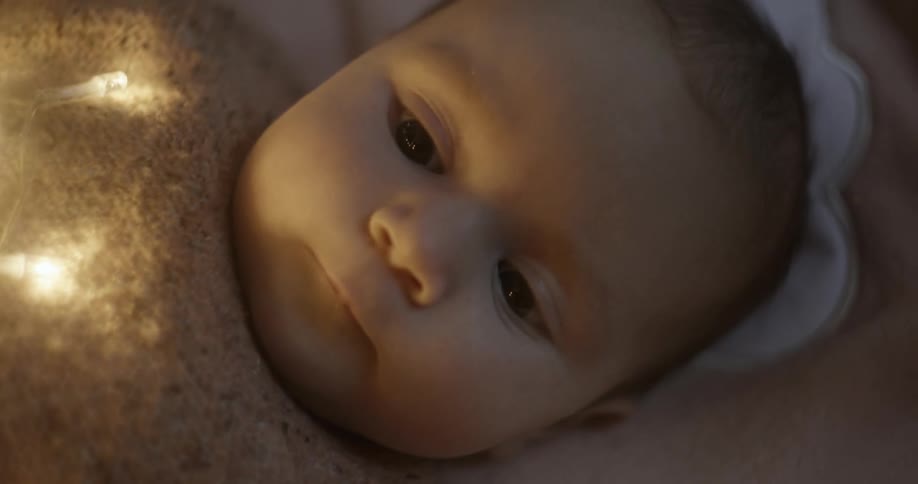 Close up of a babys face resting on bed in a dimly lit room