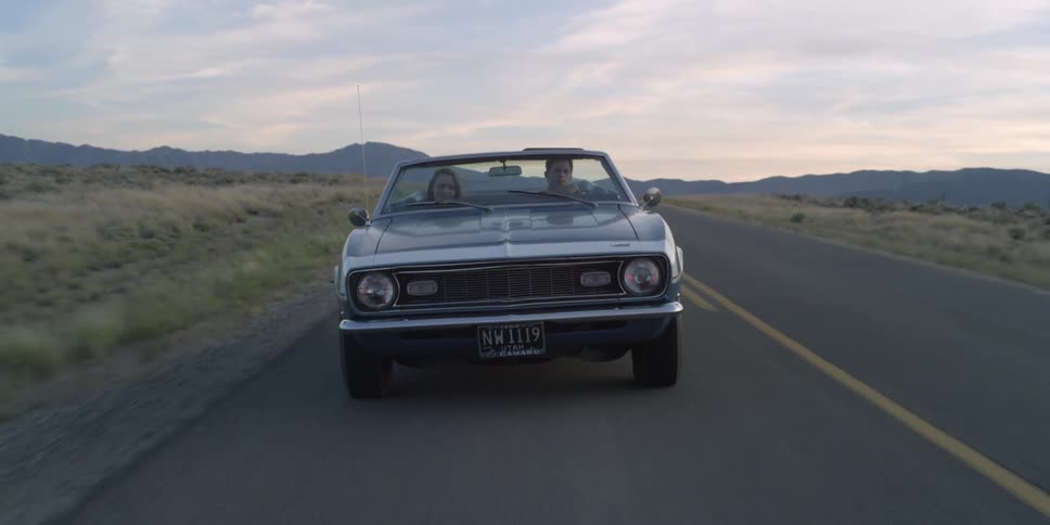 Couple driving in a convertible car on a rural road through the countryside at evening