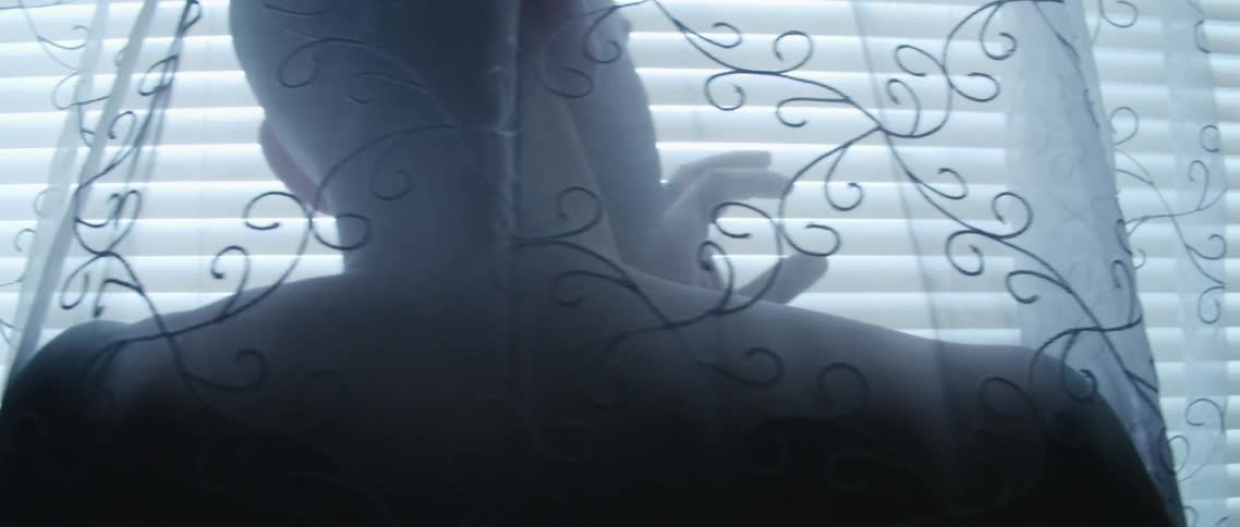 A man stands between sheer and blind and peeks through the slats