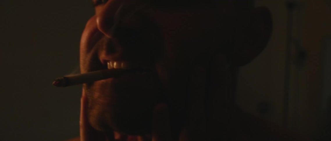 A man smiling while rubbing his face and smoking a cigarette