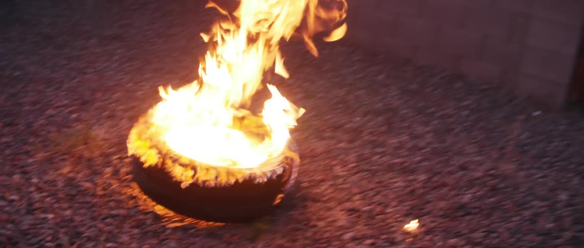 A burning tire rolling and tipping over on gravel