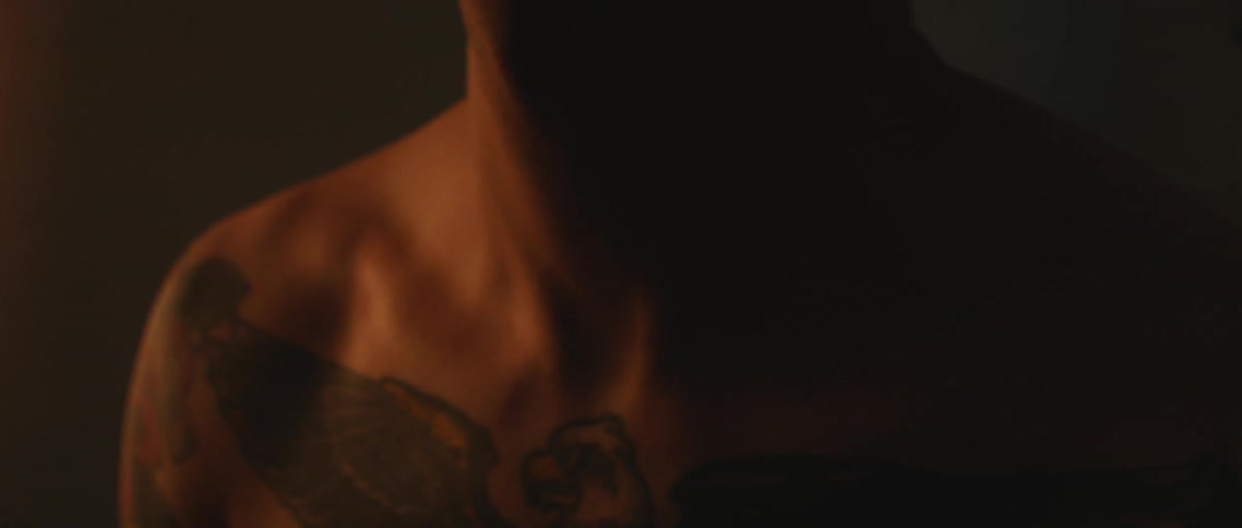 A person with a tattoo on his chest moves in the dark