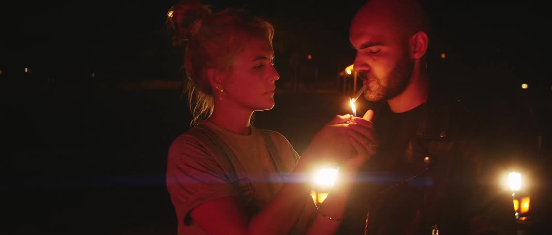 A man nods at a woman to indicate she should light his cigarette
