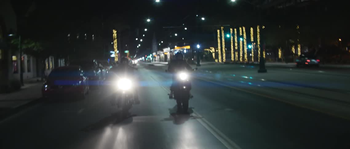 Two motorcycles with headlights on driving on the street on a town at night