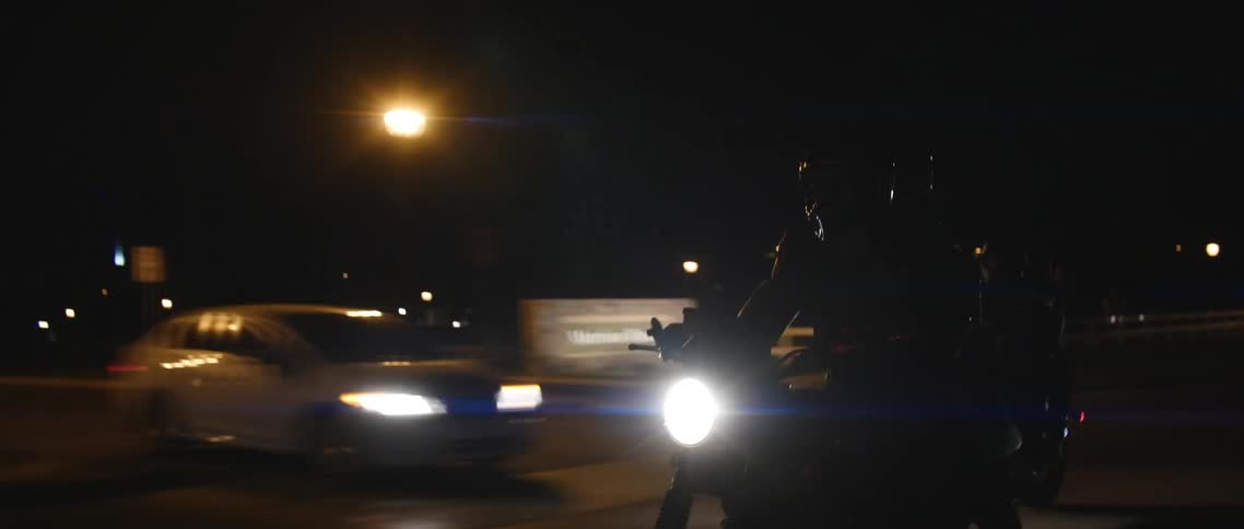 People with helmets riding on a motorcycle with headlights on a road