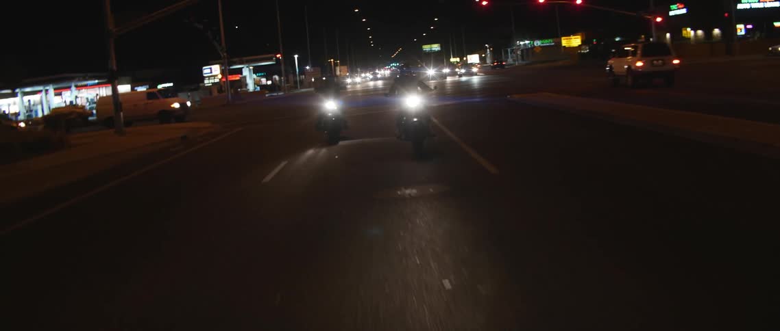 Two motorcycles with headlights on driving on the street on a town at night