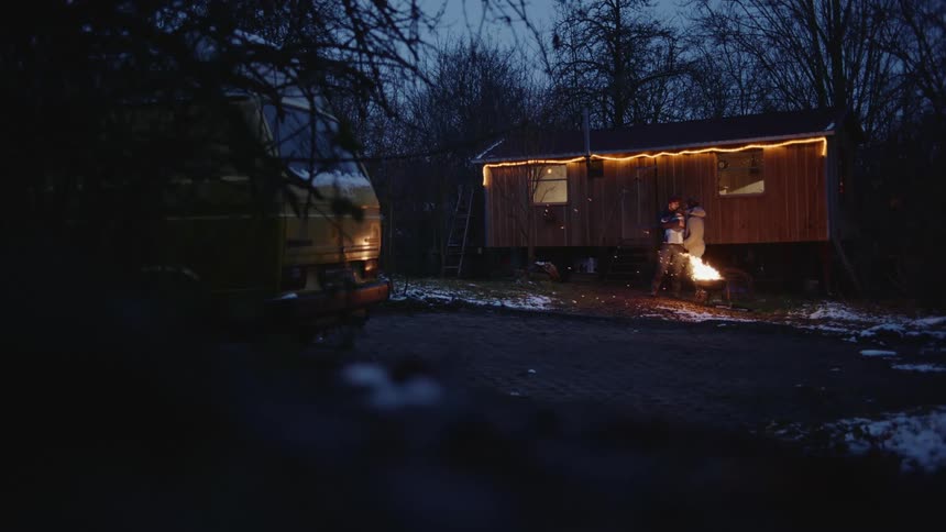 Young couple kissing in front of a fire on a camping site in the forest at winter